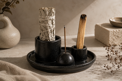 Black ceramic ritual set with holders for sage, Palo Santo and incense on a matching tray, styled in a warm neutral wellness setting.