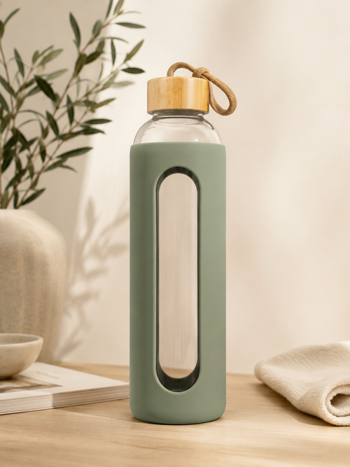 Sage green 1L glass water bottle with bamboo lid and carry loop, styled in a calm neutral wellness setting