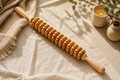Natural wooden body massage roller with 12 rotating wheels styled in a warm, calming self-care setting.